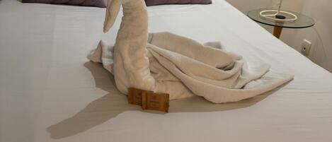 Una cama bien hecha con un cisne de toalla, dos almohadas y una lámpara de noche.
