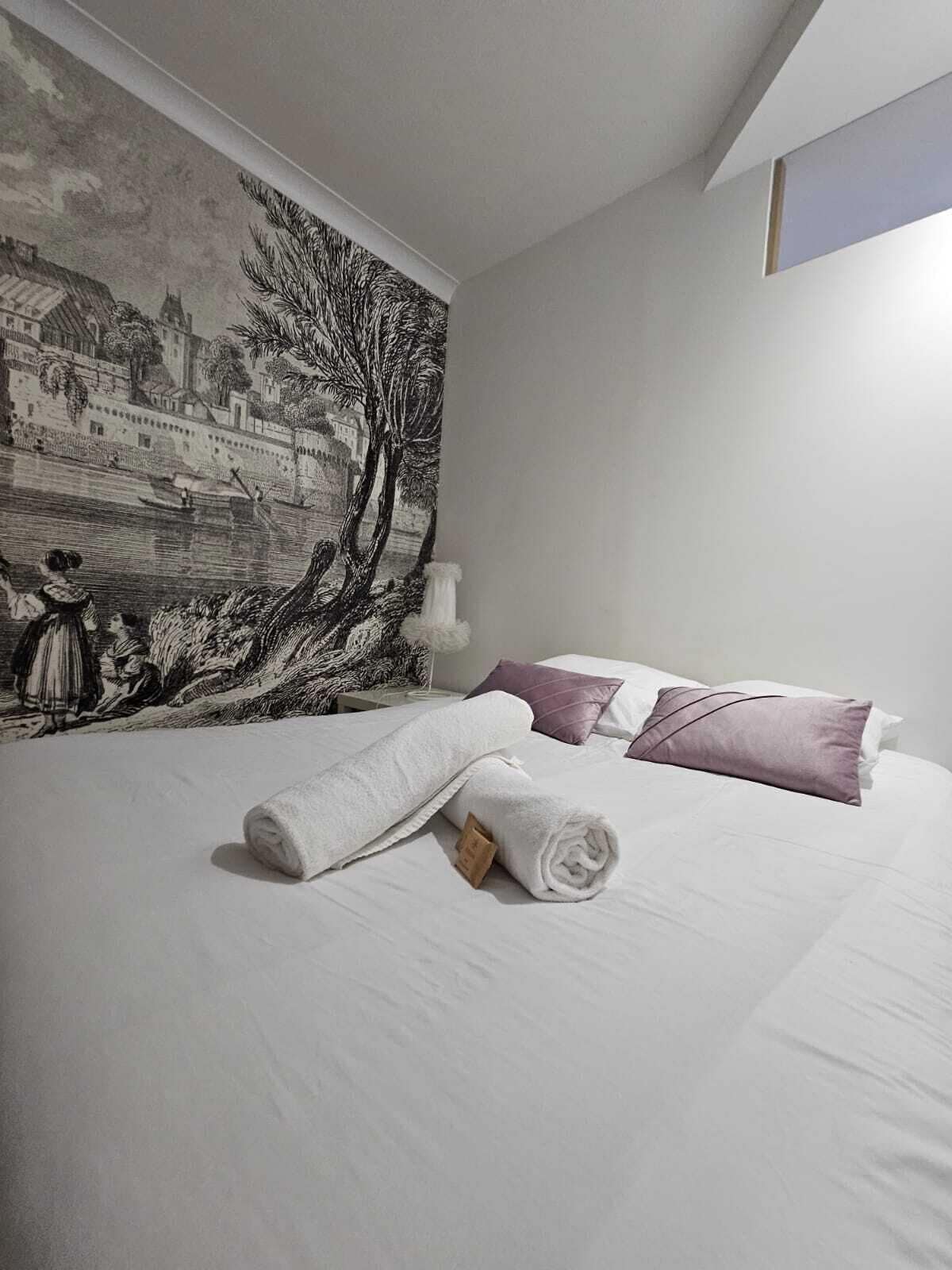 Habitación de hotel con una cama grande, ropa de cama blanca y un tapiz que representa una escena histórica.