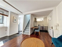 Um interior moderno com uma escada que leva a uma área de cozinha, uma mesa de jantar com cadeiras e um sofá azul.