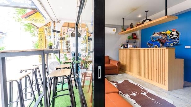 A modern hostel interior with a bar area, seating, and a view of the street. - Hip Hostel (Patong)