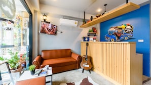A cozy room with a brown leather sofa, a wooden reception desk, and a guitar. - Hip Hostel (Patong)