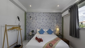 A hotel room with a bed, a wooden hanger rack, a nightstand with a lamp, and patterned wallpaper. - Hip Hostel (Patong)