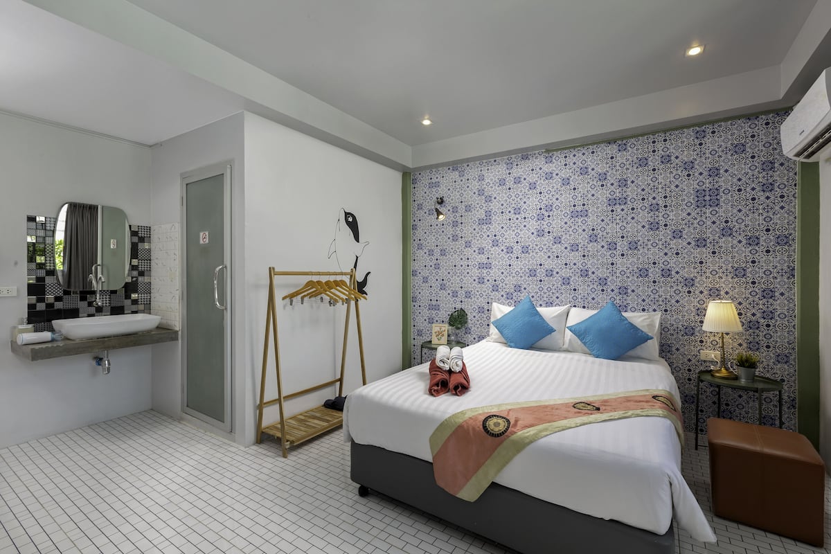 Una habitación de hotel moderna con una cama grande, un baño con lavamanos y espejo, y una pared con diseño.