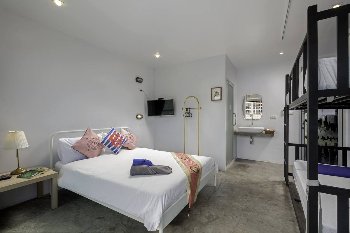 Un dormitorio con cama, mesita de noche, lámpara, televisor y un baño con lavabo y espejo.