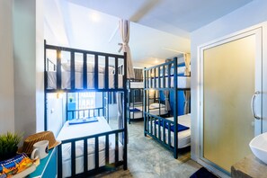 A dormitory-style room with bunk beds, a desk with a laptop, a plant, and a shower area. - Hip Hostel (Patong)