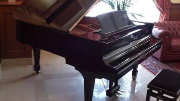 A grand piano in a well-lit room with a tiled floor, a small table, and a chair.