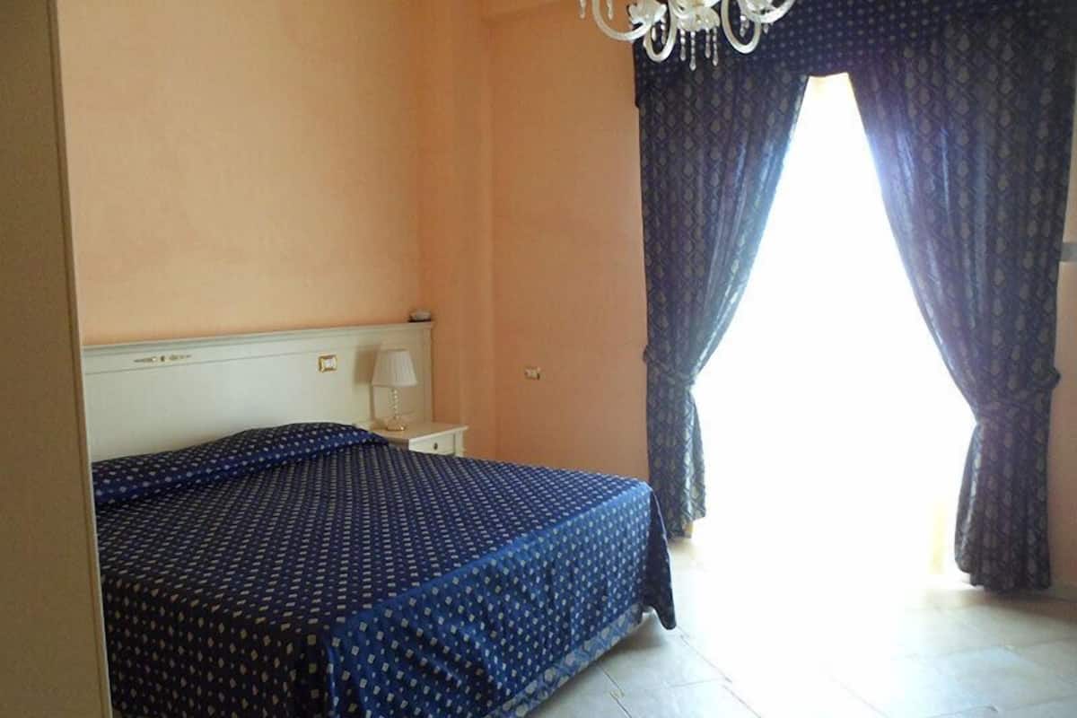 A bedroom with a bed, a nightstand, a lamp, and a window with curtains.