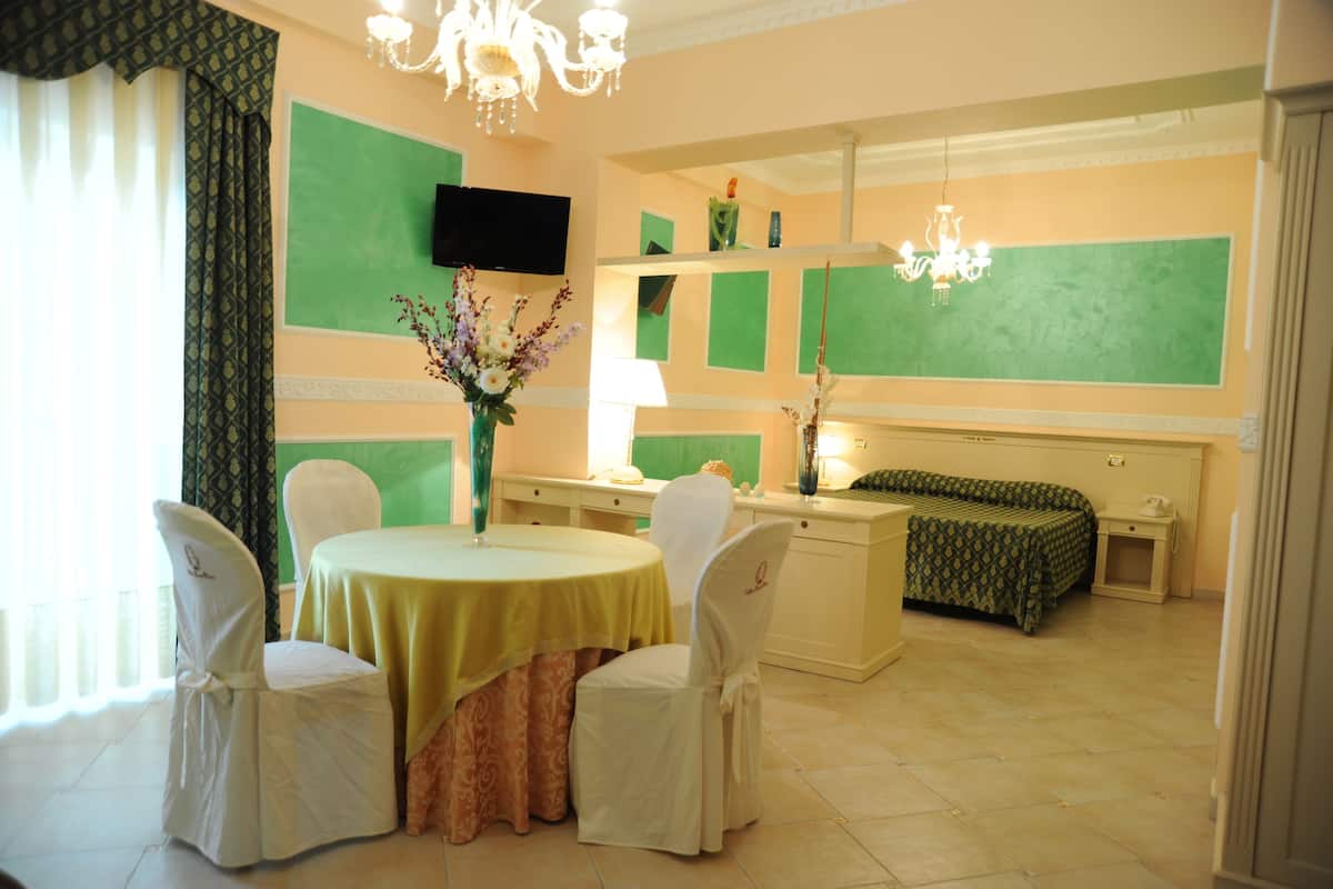 A hotel room with a dining area, a bed, a TV, and a chandelier.