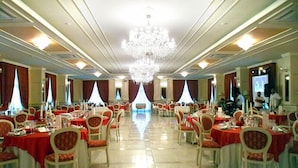 Une salle de banquet avec des rangées de tables, des chaises et un lustre.