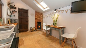 Un'accogliente zona pranzo con tavolo, sedie, una TV a parete e un caminetto con parete in mattoni e luci decorative.