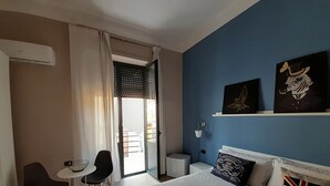 Habitació d'hotel amb llit, escriptori, cadira, taula petita i finestra amb cortines.
