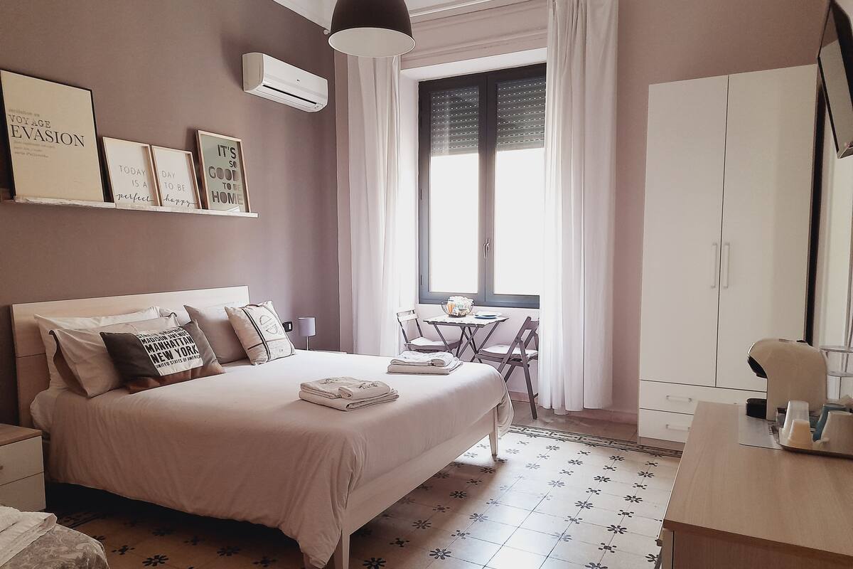 Un dormitorio ordenado con cama, mesita de noche y una pequeña mesa con sillas.