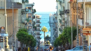 Un carrer flanquejat per edificis, una palmera al centre i una vista del mar al fons.
