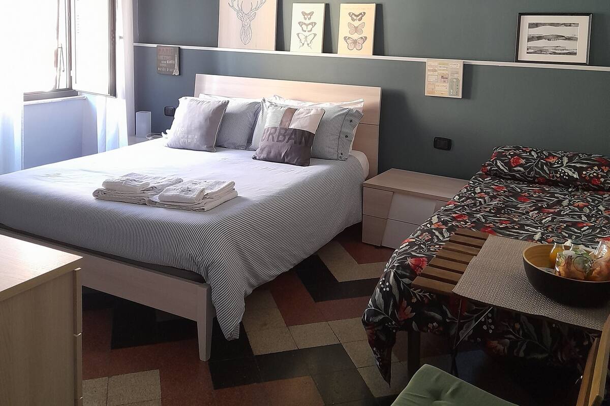 Un dormitorio con cama, mesitas de noche, un escritorio y una ventana con cortinas.