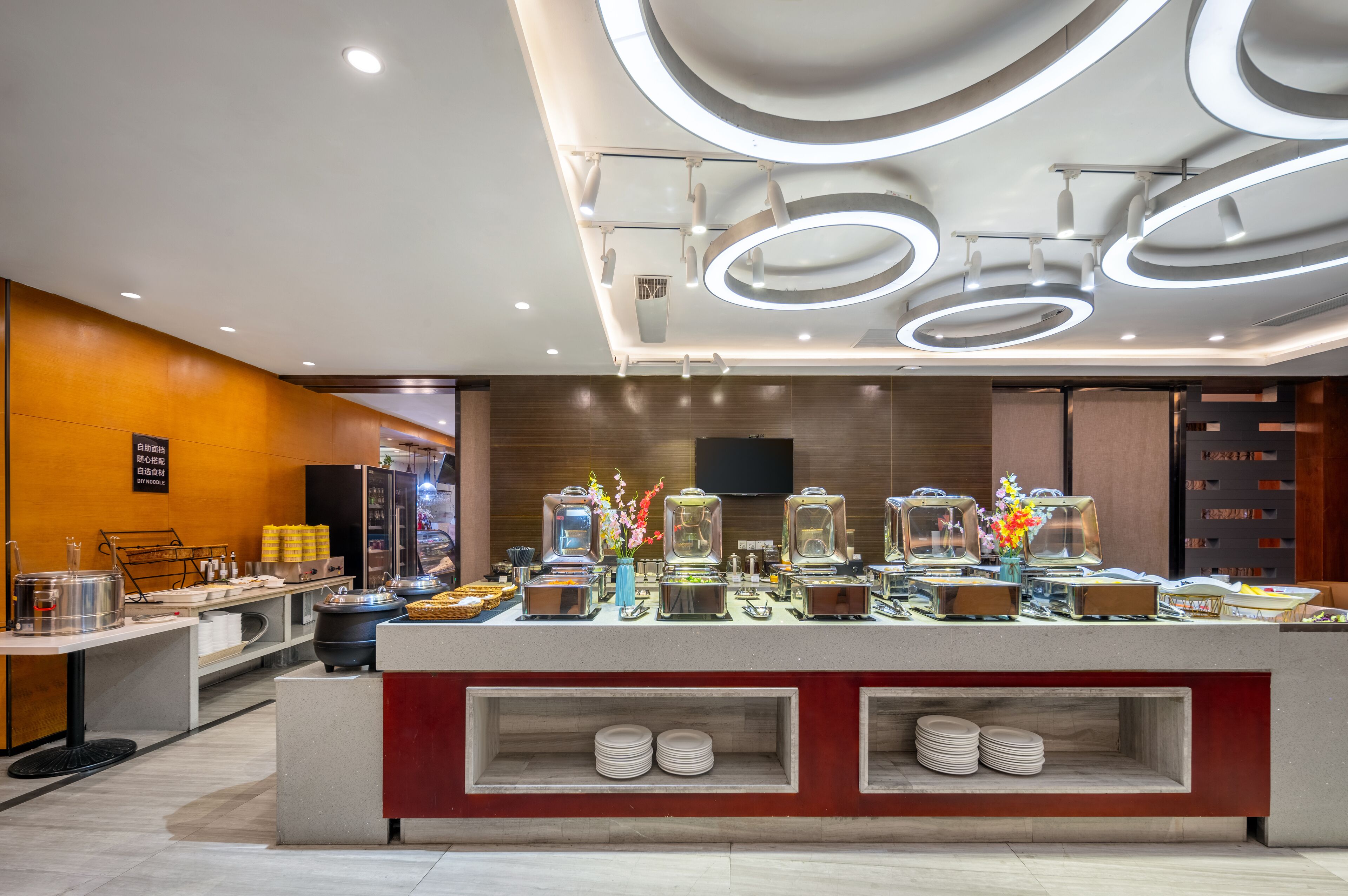 A buffet area with various food stations, a modern ceiling design with circular lights, and a clean, organized layout.