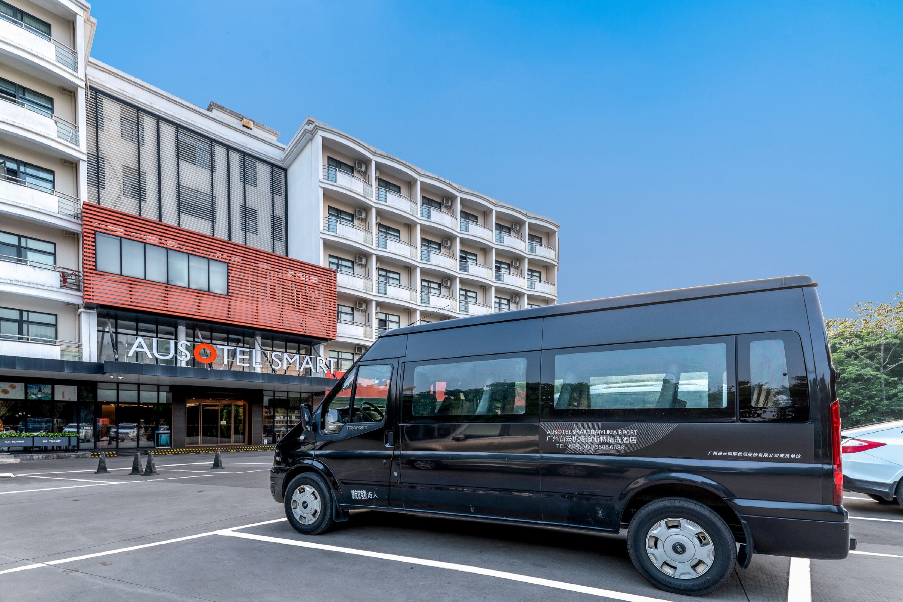 Una camioneta negra estacionada frente a un hotel con fachada moderna, ventanas grandes y un letrero visible del hotel.