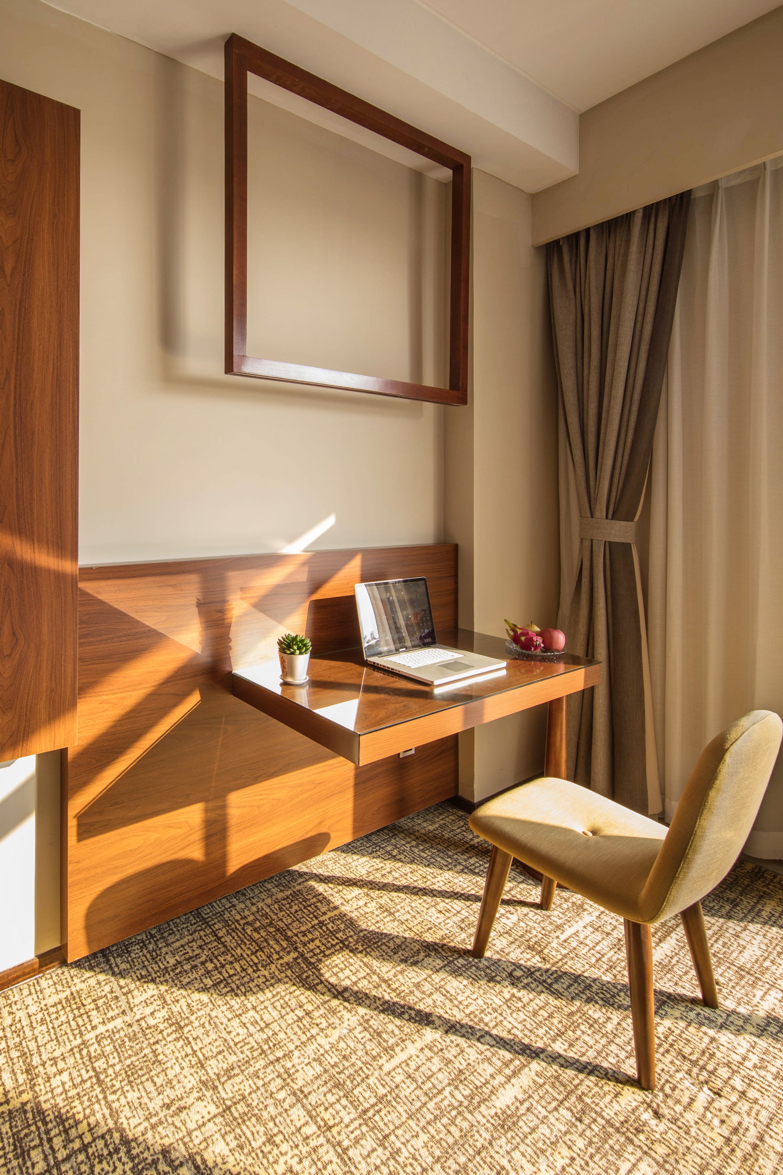 A hotel room with a wooden desk, a laptop, a small potted plant, and a chair.
