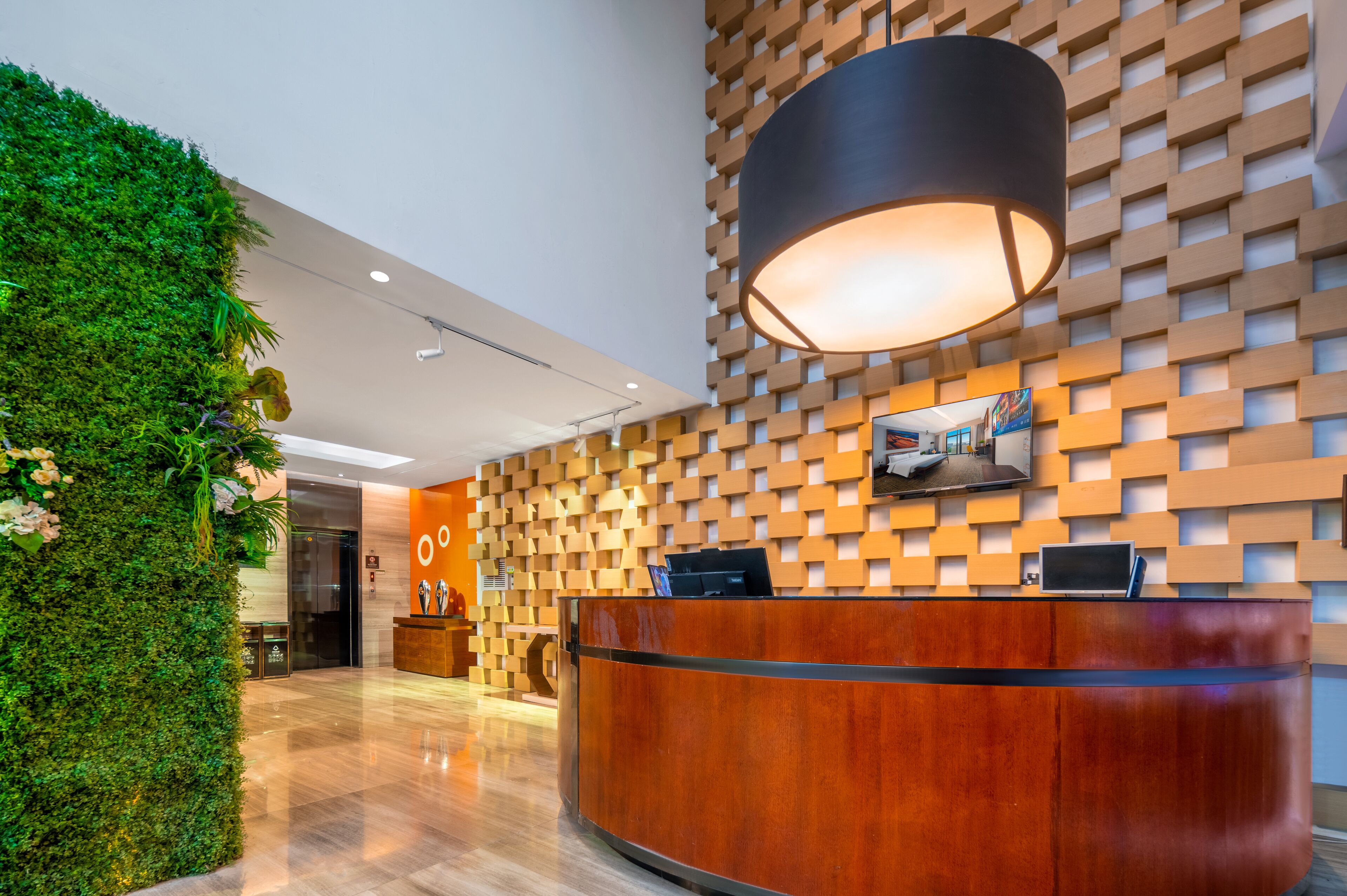 A reception area with a wooden reception desk, a large wall-mounted lamp, and a green vertical garden.