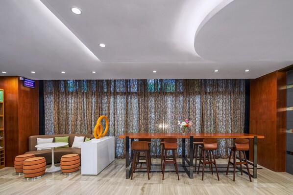 A modern interior with a wooden reception desk, a white sofa, and a bar area with stools.