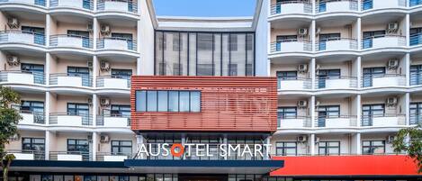 A multi-story hotel with a modern facade, balconies, and a prominent signage for "AUSOTEL SMART".