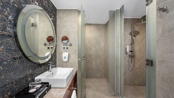 A modern bathroom with a large oval mirror, a rectangular sink, a glass-enclosed shower, and a marble-tiled wall.