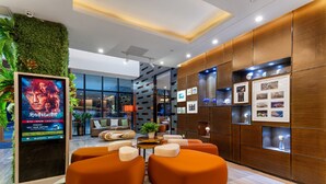 A modern lobby with orange seating, a digital screen, wooden paneling, and framed pictures.