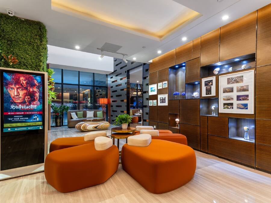 A modern lobby with orange seating, a digital screen, wooden paneling, and framed pictures.