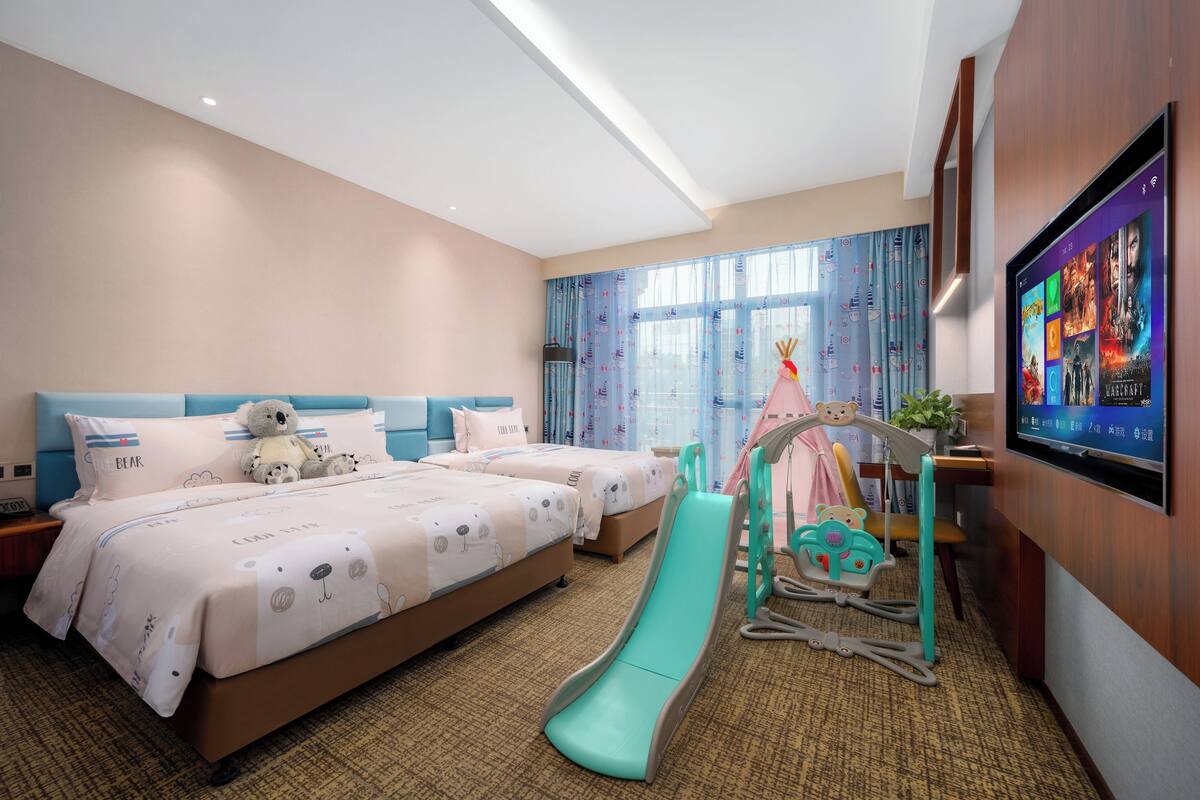 A hotel room with two beds, a slide, a play area, and a TV on the wall.