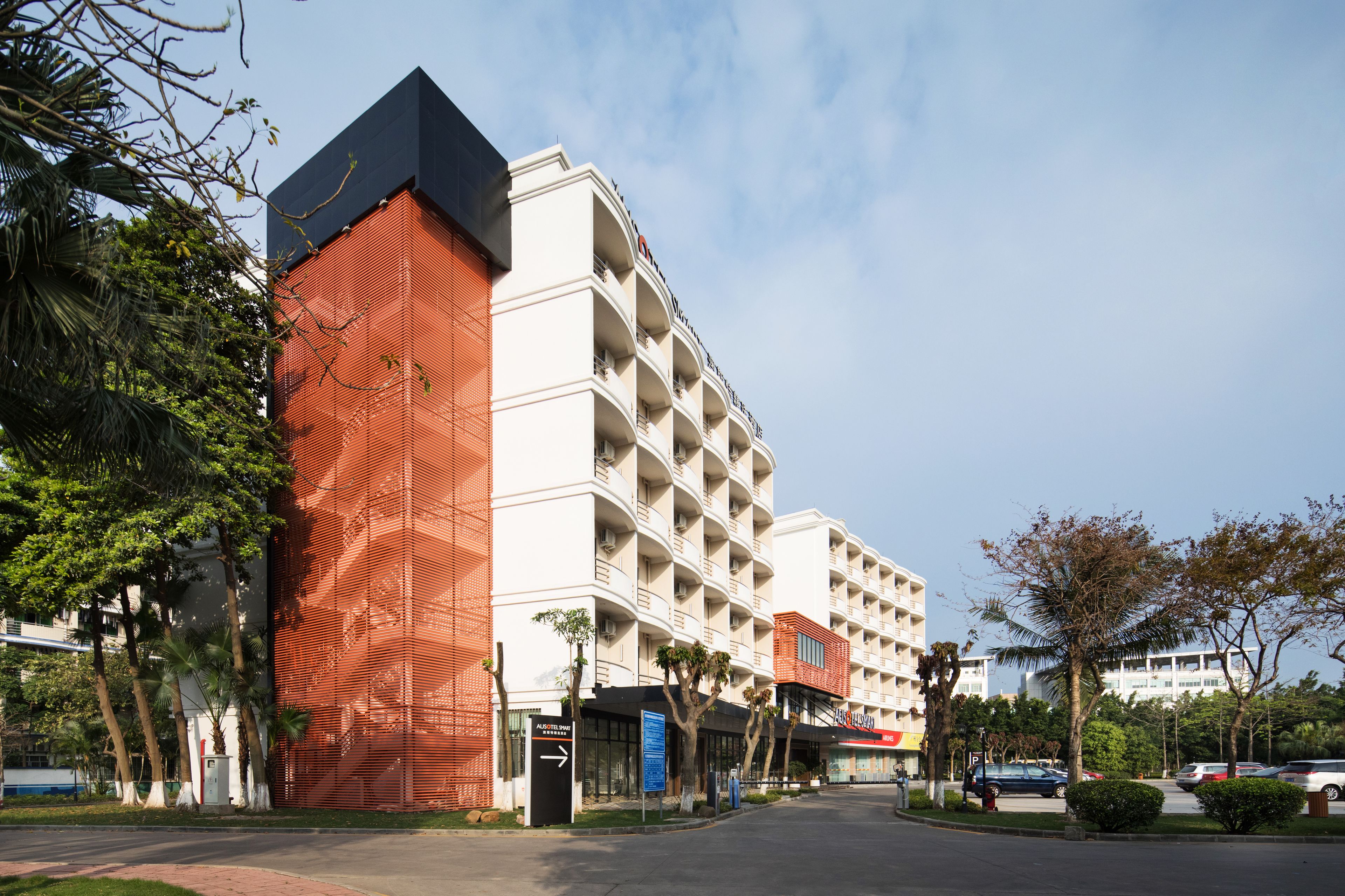 A multi-story hotel with a modern architectural design, featuring balconies and a prominent red facade.
