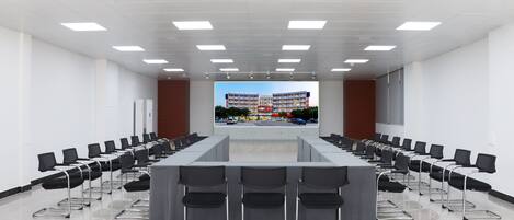 A conference room with a long table and chairs, white walls, and a view of a building through a window.