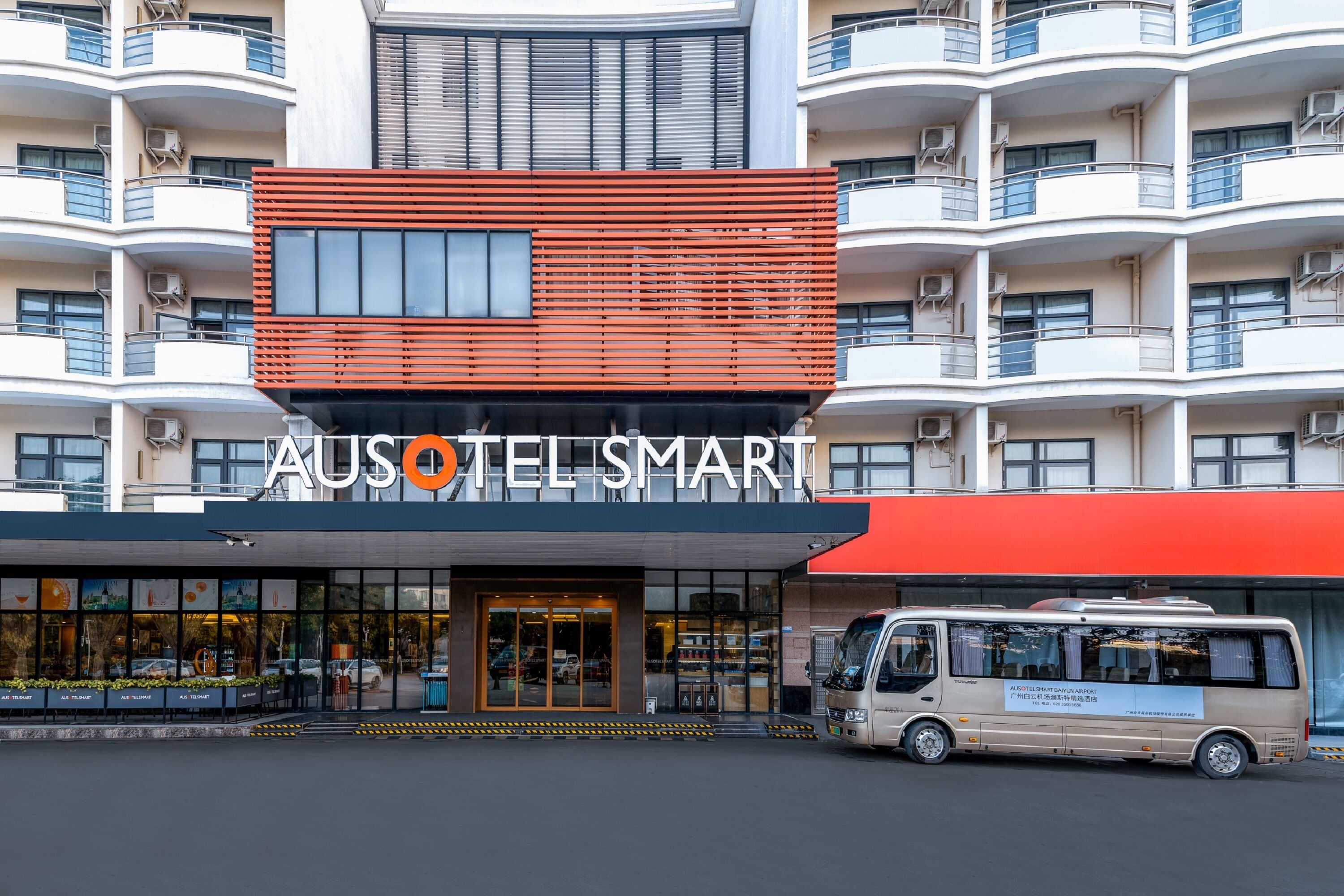 Un hotel con fachada moderna, varios balcones y una furgoneta estacionada frente a él.