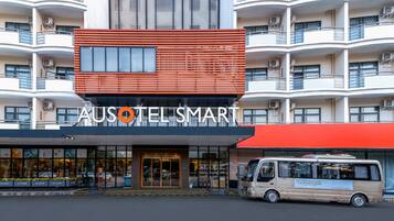 Un hotel con fachada moderna, varios balcones y una furgoneta estacionada frente a él.