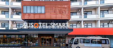 Un hotel con fachada moderna, varios balcones y una furgoneta estacionada frente a él.