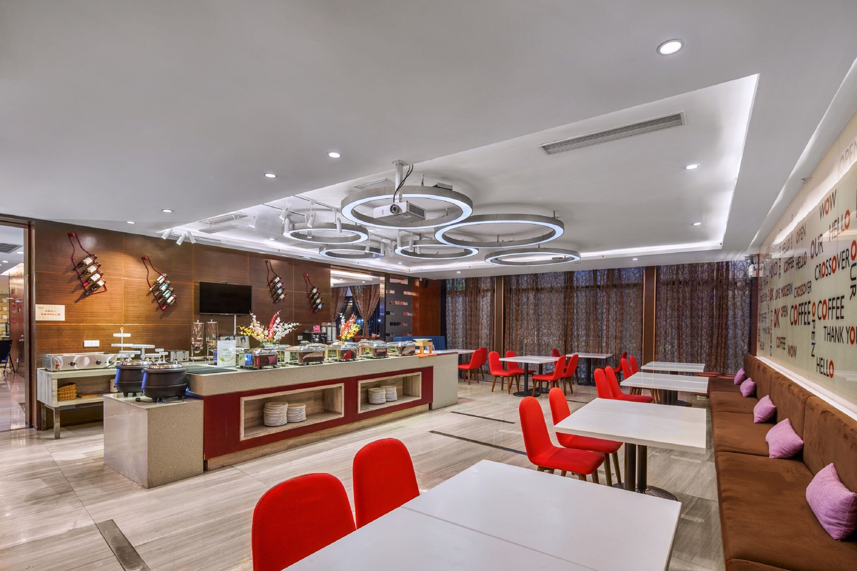 A modern restaurant with a central counter, red chairs, and a brown sofa with purple cushions.