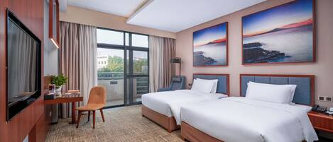 Habitación de hotel con dos camas, un escritorio con silla, televisor y ventanas amplias con cortinas.
