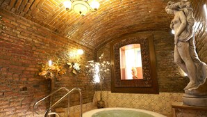 Une salle de spa avec un plafond en briques, une statue en pierre, une baignoire et un miroir décoratif.