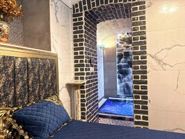 Quarto luxuoso com cabeceira de mármore, cama acolchoada azul, pequena mesa de mármore e uma cascata na parede.