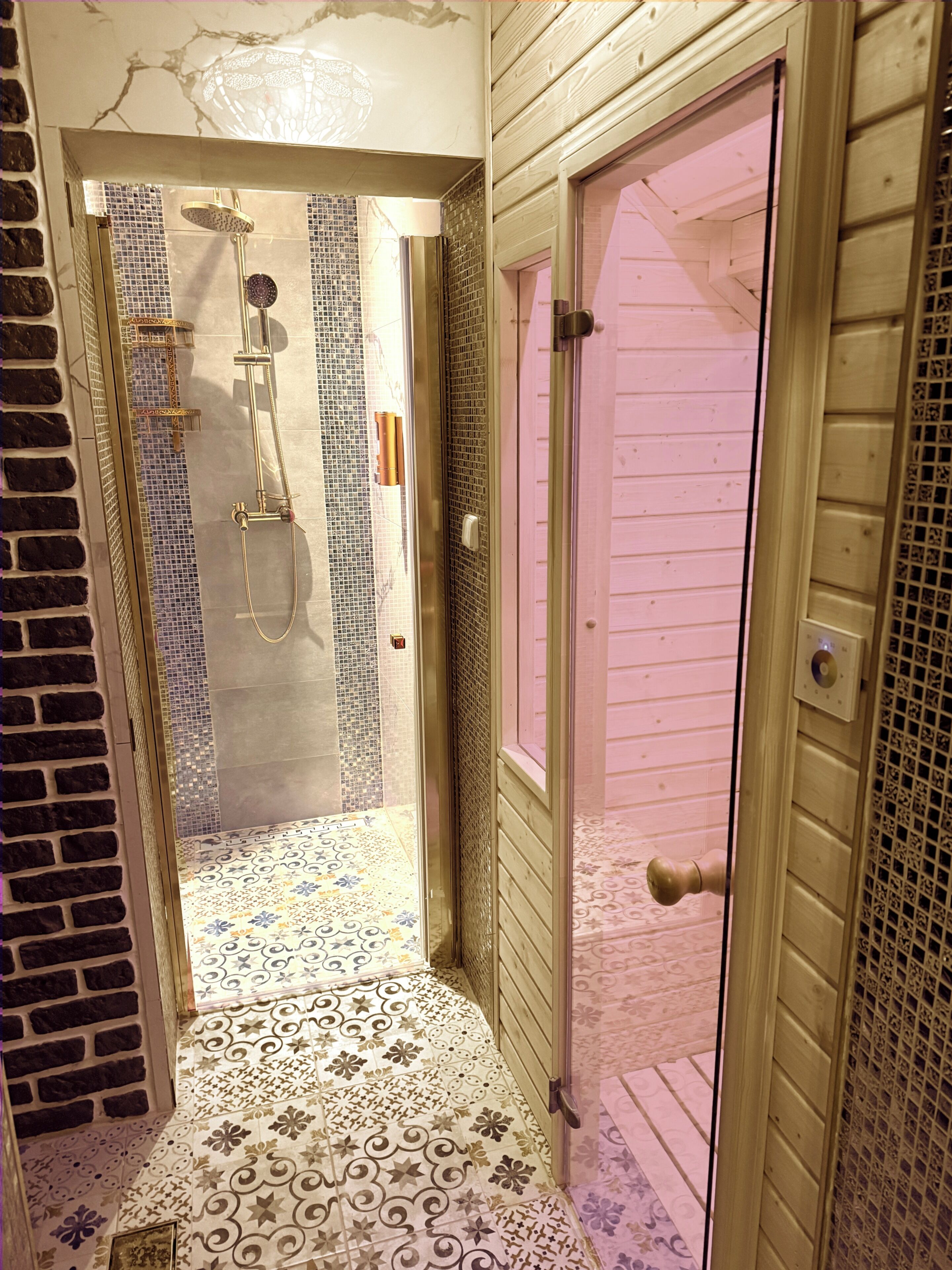 Baño con ducha, paredes de azulejos y suelo estampado.