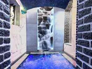 A spa area with a waterfall feature, a hot tub, and stone walls.