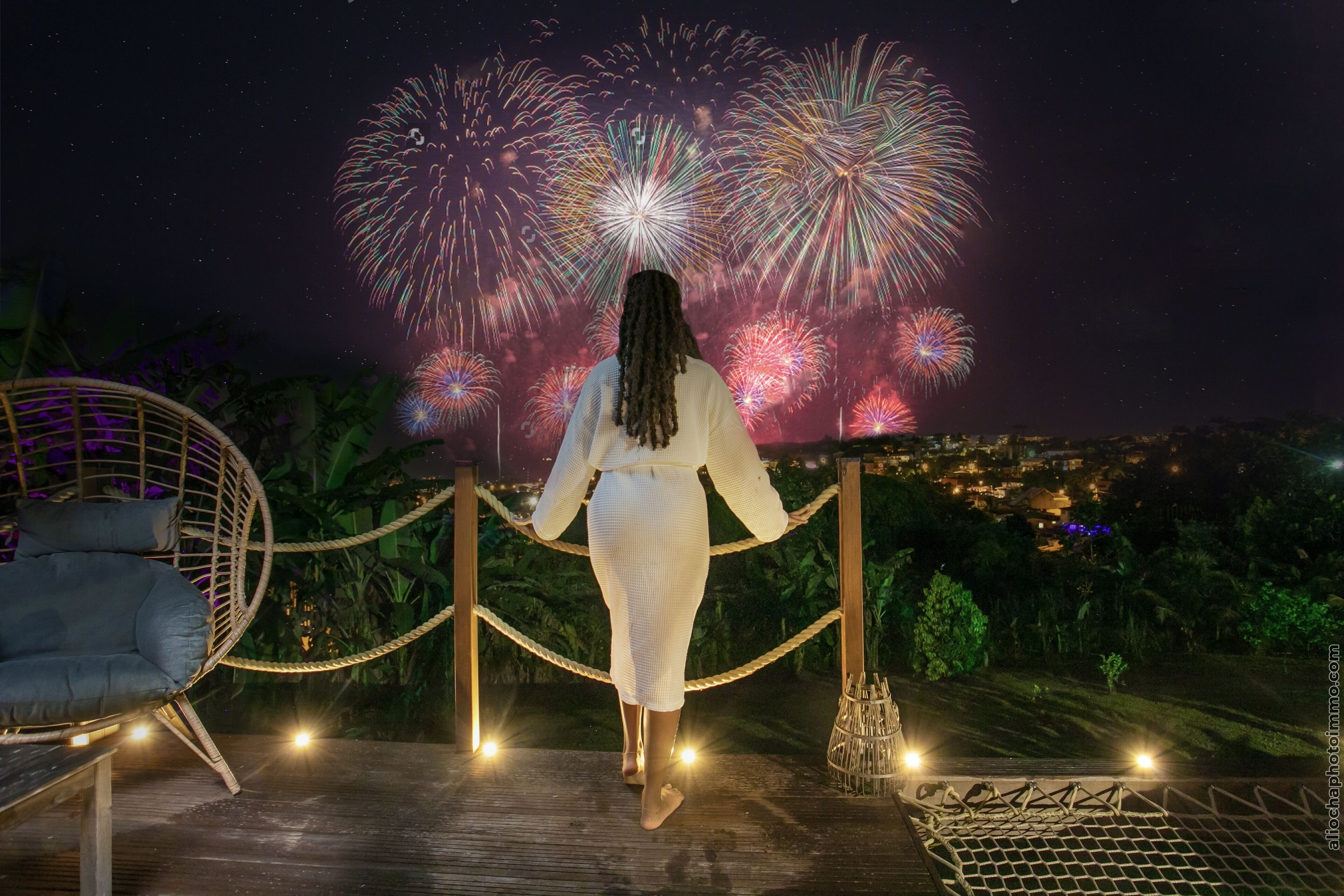 A person standing on a wooden deck with a view of fireworks in the night sky.