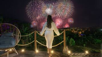 A person standing on a wooden deck with a view of fireworks in the night sky.