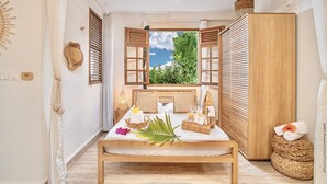 A bedroom with a bed, wooden headboard, and a view of greenery outside. - Créole Bay - Suites and Spa (Fort-de-France)