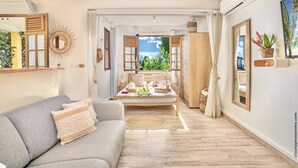 A modern living room with a sofa, a wooden bed, and a view of the outdoors. - Créole Bay - Suites and Spa (Fort-de-France)