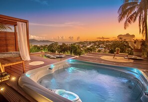A hot tub on a wooden deck with a view of a cityscape and mountains at sunset. - Créole Bay - Suites and Spa (Fort-de-France)
