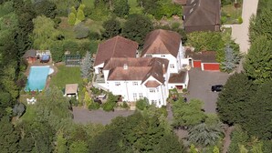 A large white house with a swimming pool, surrounded by dense greenery and trees. - The Pines Hotel (Slough)