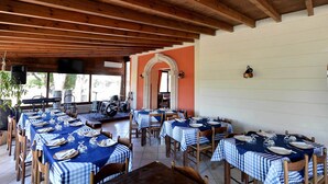 A restaurant with multiple tables set for dining, wooden beams on the ceiling, and a large arched doorway. - Agriturismo Santa Chiara (Alezio)