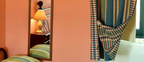 A room with a bed, a mirror, and a window with striped curtains.