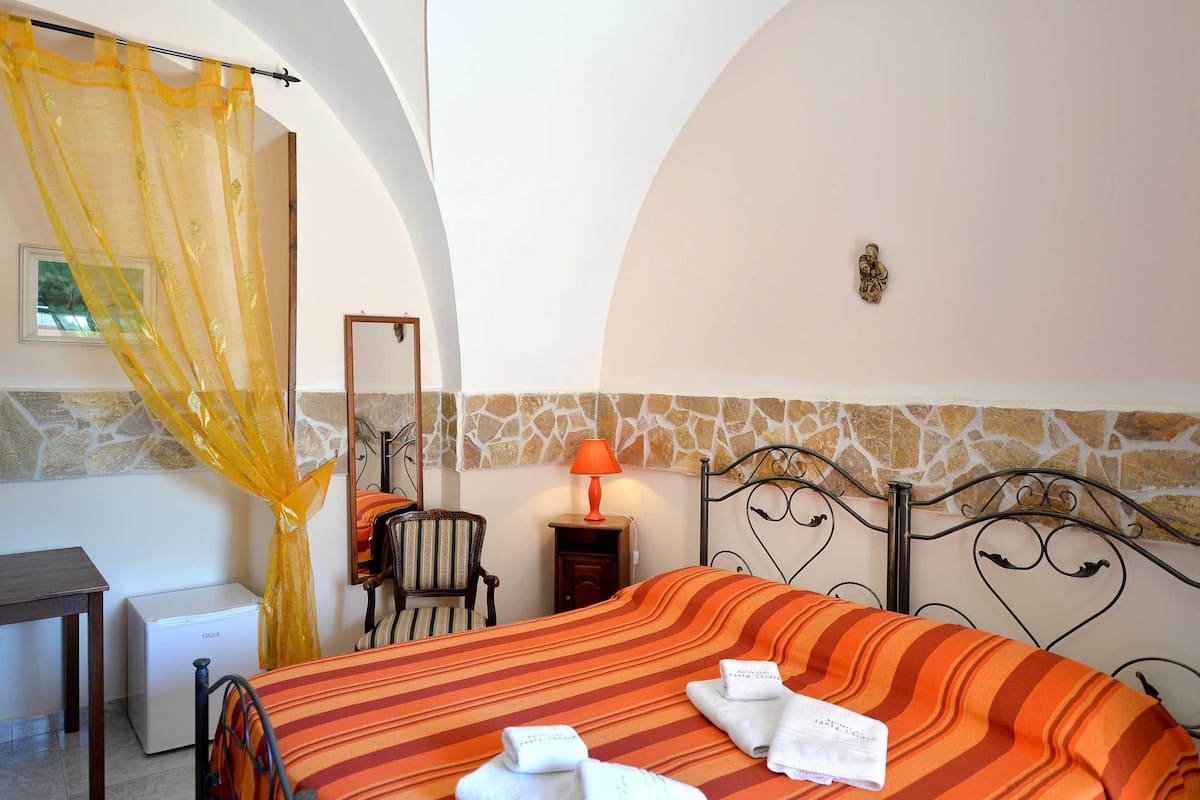A hotel room with a bed, a chair, a table, a lamp, and a curtain.