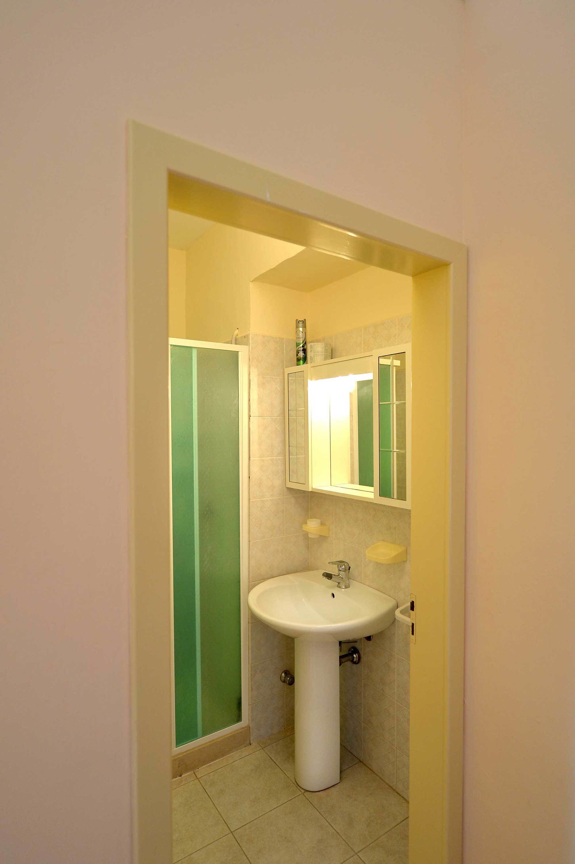 A bathroom with a white sink, green-tinted shower enclosure, and a mirror above the sink.