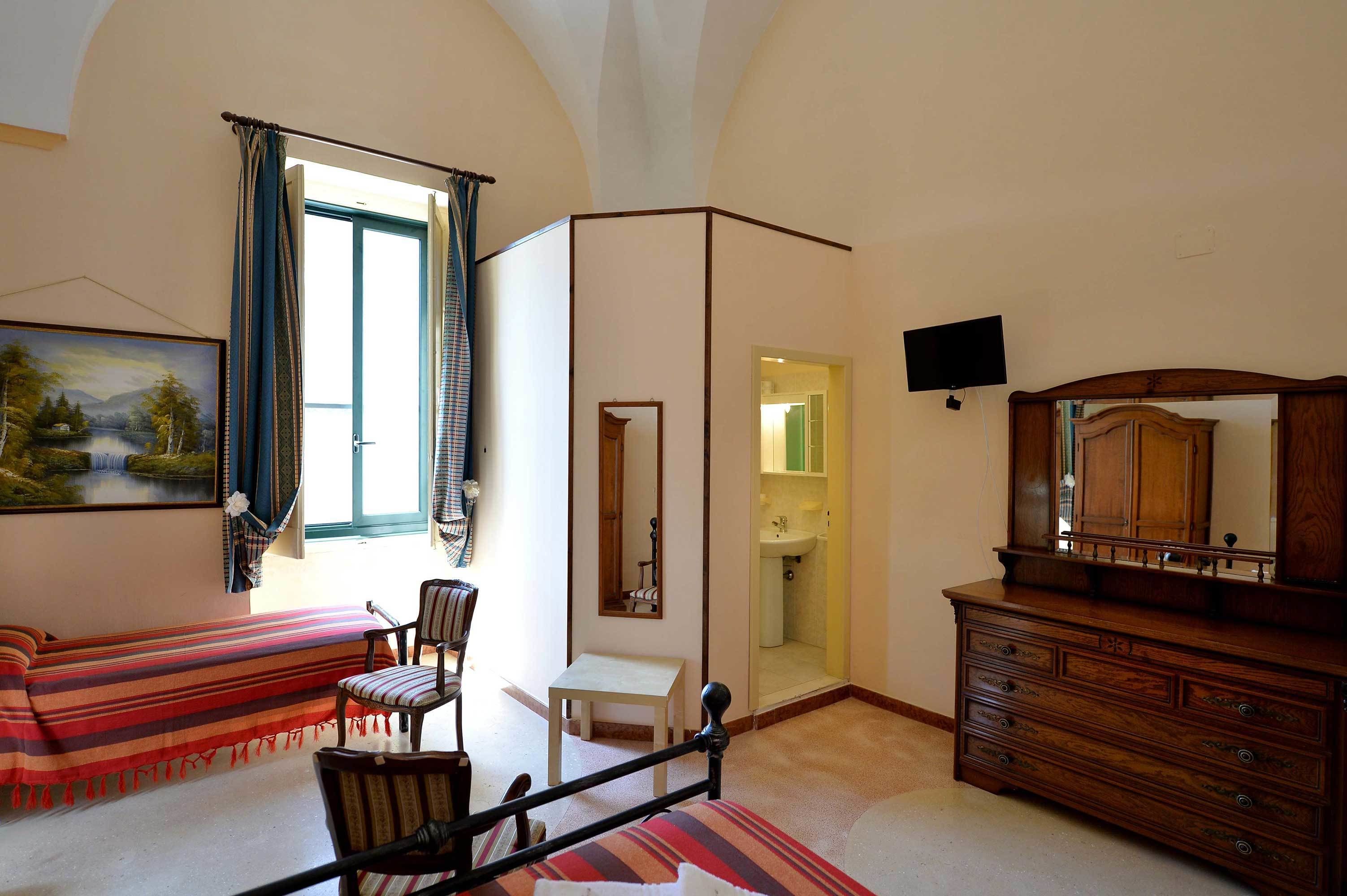 A room with a bed, a chair, a dresser, a television, and a bathroom door.